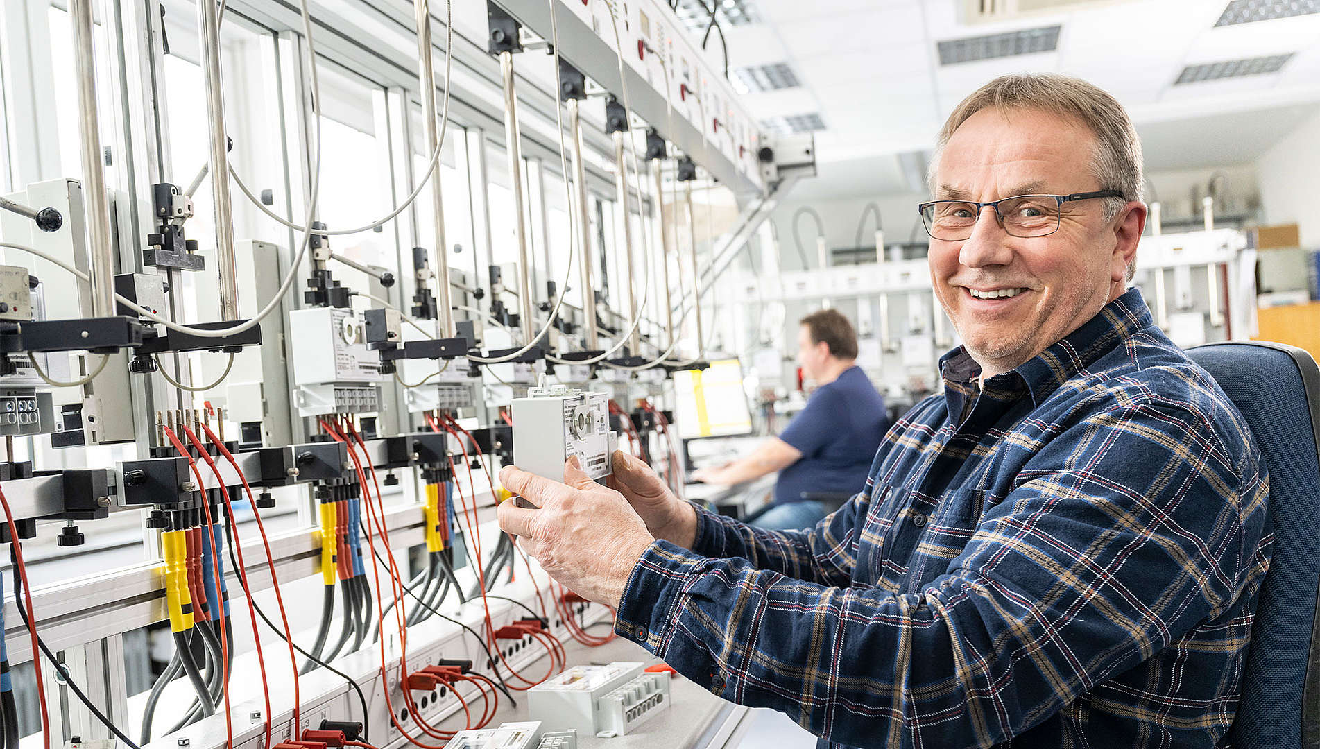Eine Person sitzt in der Prüfstelle Strom mit einem Zähler in der Hand und lächelt freundlich.