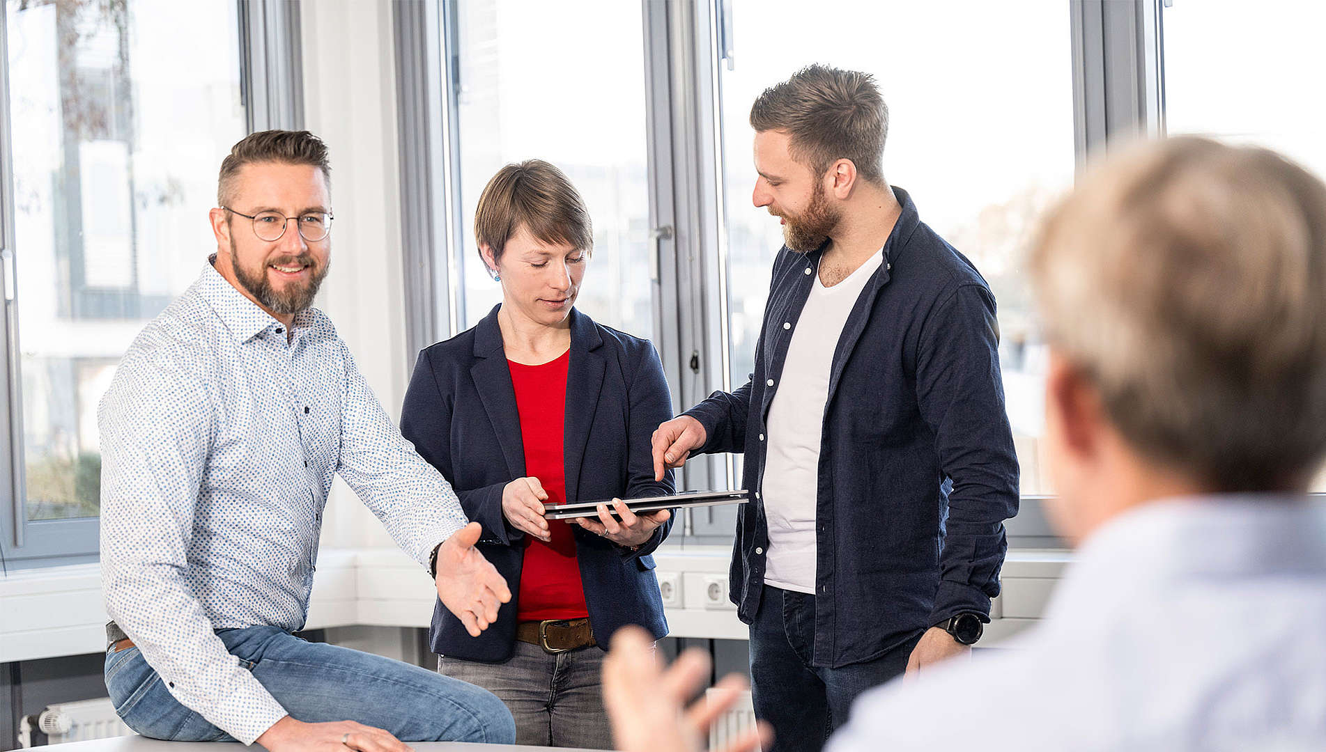 Mehrere Personen sind im Gespräch. Zwei Personen schauen auf ein Tablet und erklären etwas.
