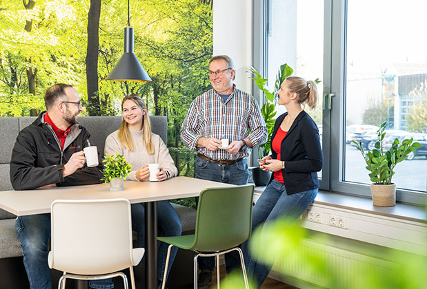 Mehrere Personen stehen im Pausenraum am Tisch und unterhalten sich.