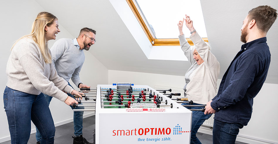 Vier Personen stehen am smartOPTIMO-Kicker. Eine Frau jubelt und freut sich über den Sieg.